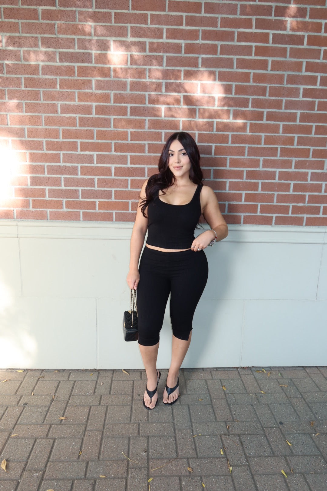 Front view of a model wearing a black ribbed tank and capri set